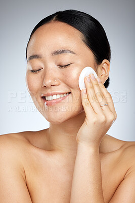 Buy stock photo Skincare, asian and woman cleaning face with soft cotton pad for healthy and fresh skin routine. Hygiene, natural and beauty of girl with cosmetics removal swab on grey studio background.

