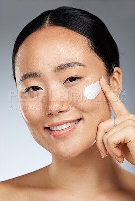 Buy stock photo Beauty, skincare and face, cream and woman apply moisturizing product and natural cosmetics, facial treatment in portrait. Asian, model and smile, skin and body care, glow with studio background.
