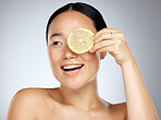 Portrait, happy and woman using lemon for facial skincare cleaning, vitamin c and cosmetic benefits in studio in Tokyo. Smile, fruit and young Asian beauty model cleaning a glowing face for wellness
