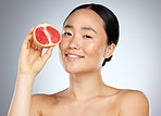 Grapefruit, skincare and woman with food for face, wellness and beauty against a grey mockup studio background. Portrait of young, happy and Asian model with fruit for nutrition, diet and body health