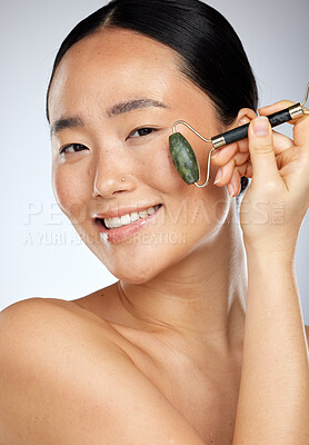 Buy stock photo Asian woman, cosmetics and facial roller for wellness, skincare and smooth face with studio background. Young female, girl and anti aging for natural beauty, smile and happy for health and body care.