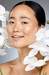 Beauty, skincare and flowers with a model asian woman posing in studio on a gray background for health or wellness. Face, portrait and natural with an attractive female posing to promote a product