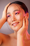 Beauty, makeup and cosmetic of a woman model from Korea with a smile. Cosmetics, happy and calm young person face posing with hands to show skin wellness, skincare with creative pink studio light