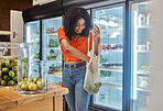 Shopping, fruits and customer black woman in supermarket at vegetables fridge for vegan, nutrition and healthy food. Happy woman at supermarket or eco friendly marketplace and grocery sustainable bag