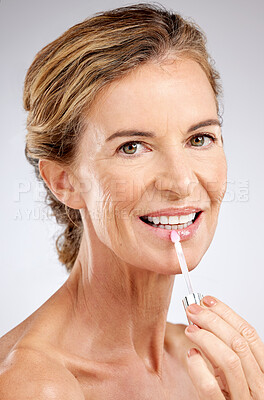 Buy stock photo Cosmetics, lip gloss and senior woman for wellness, natural beauty and healthy with grey studio background. Portrait, makeup and elderly female with smile, confident and happy with hydrate product.