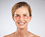 Face, beauty and antiaging with a senior woman using under eye patch cosmetics for skincare in studio on a gray background. Portrait, treatment and product with a mature female posing for wellness