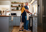 Senior couple in kitchen hug, cooking healthy food together and care in retirement lifestyle. Elderly man and woman with apron, hugging wife in home or love nutrition dinner meal with happy and smile