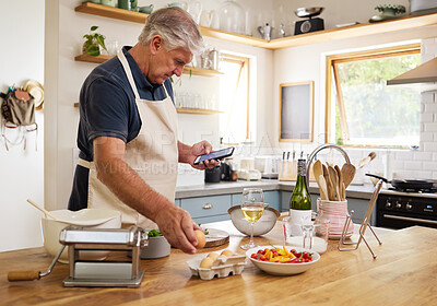 Buy stock photo Senior man, cooking and phone for recipes, research or ingredients for the perfect meal in the kitchen at home. Elderly male cook or baker with food browsing online recipe or streaming on smartphone