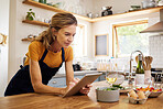 Woman, tablet and kitchen for online recipe, browsing or research in cooking or baking at home. Female with apron checking instructions on the internet for meal or ingredients on touchscreen indoors