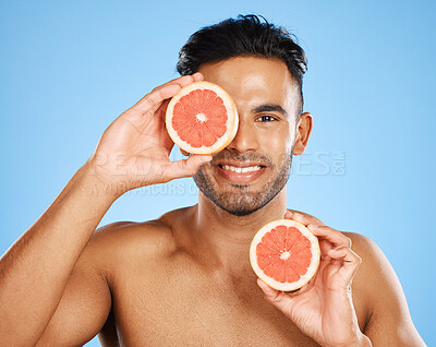 Buy stock photo Beauty, grapefruit and skincare with a man model in studio on a blue background to promote natural treatment. Food, wellness and portrait with a handsome young male holding a fruit slice to his face