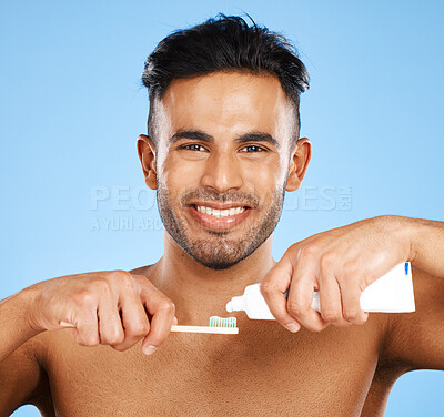 Buy stock photo Mouth, dental and man brushing teeth in studio for wellness, health and grooming on blue background. Portrait, face and teeth of indian guy happy with oral cleaning product, toothpaste and mockup