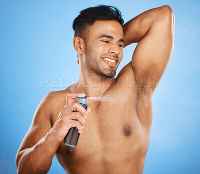 Buy stock photo Smile, happy and man spray deodorant for hygiene, fresh scent or body care after shower on blue studio background. Perfume, product and male model from India spraying armpit to prevent smell or odor
