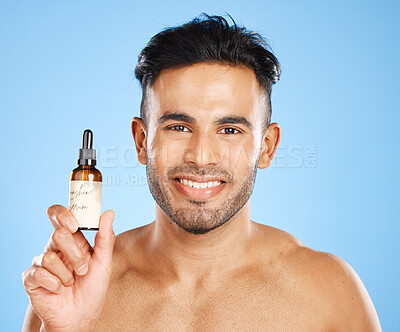 Buy stock photo Indian man, serum and skincare with smile for natural beauty, organic facial and wellness with blue studio background. Body care, male and with cosmetic oil for smooth skin, glow and happy to hydrate