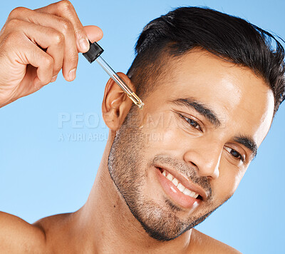 Buy stock photo Oil, skincare and man with serum for face against a blue studio background. Wellness, happy and young model with a liquid with hyaluronic acid for growth of beard, cleaning and dermatology health