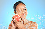 Skincare, beauty and woman with grapefruit in studio for cleaning, grooming and wellness against blue background. Face, water and fruit product with girl skin model relax, smile and facial, treatment