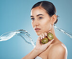 Beauty, water and kiwi with a model woman in studio on a blue background for skincare or wellness. Fruit, luxury and health with a young female posing to promote a healthy diet or natural lifestyle