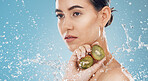 Beauty, water and kiwi with a model woman posing in studio on a blue background for natural skincare with a splash. Food, wet and luxury with an attractive female posing to promote health or wellness