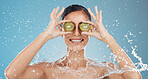 Skincare, water and woman in studio with kiwi for cleaning, wellness and health against blue background mockup. Shower, fruit and girl model happy, smile and relax with green skin product for beauty