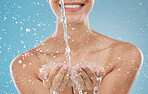 Skincare, water and hands on blue background in studio for hydration, refreshing and facial cleanse. Splash, wellness and woman ready to clean face for washing, moisturizing and hydrate healthy skin 