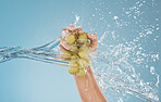 Hand, grapes and water by woman in studio for wellness, health and nutrition mockup, studio and blue background. Splash, fruit and model hands for plant, organic and nutrition skin, product and diet 