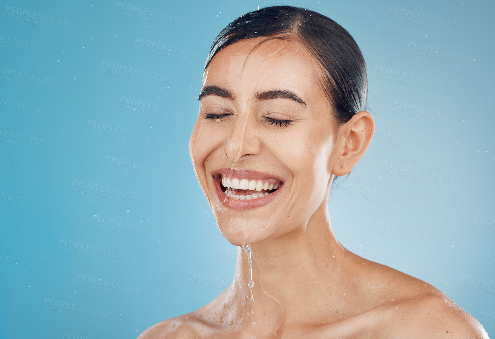 Buy stock photo Skincare, cleaning and washing face by woman in studio for wellness, shower, happy and relax against a blue background mockup. Girl, water and face with model face wash for beauty, splash and skin