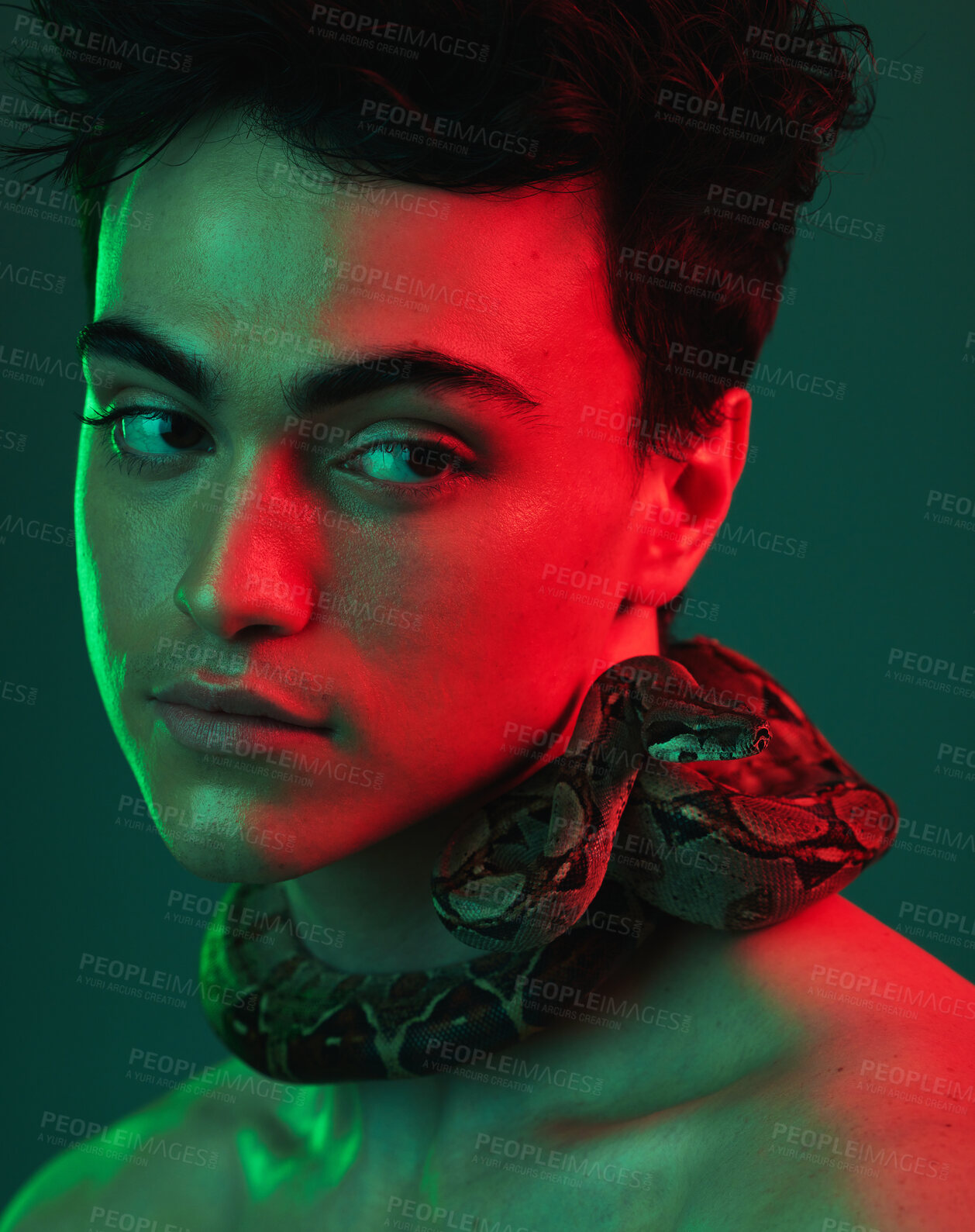 Buy stock photo Beauty, snake and model in a studio with neon light of green and red color posing with a serpent. Skincare, face and man from Mexico standing with a reptile on his neck isolated by a green background