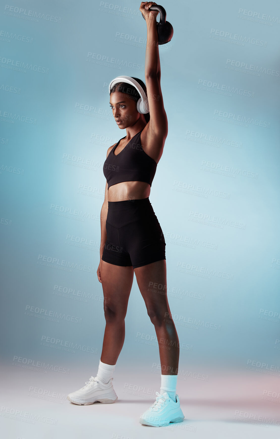 Buy stock photo Health, exercise and woman in headphones with kettlebell on a blue studio background. Fitness, sports and female from India streaming music, radio or podcast while training with exercising weight.