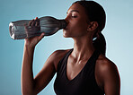 Fitness, sports and woman drinking water in studio for a healthy body after training, cardio workout and exercise. Wellness, blue background and thirsty girl enjoys a beverage to hydrate or hydration