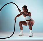 Woman, battle rope and exercise on blue background in studio resistance training, energy sports or cardio workout. Personal trainer, fitness model or person with wellness health goals for arm muscles