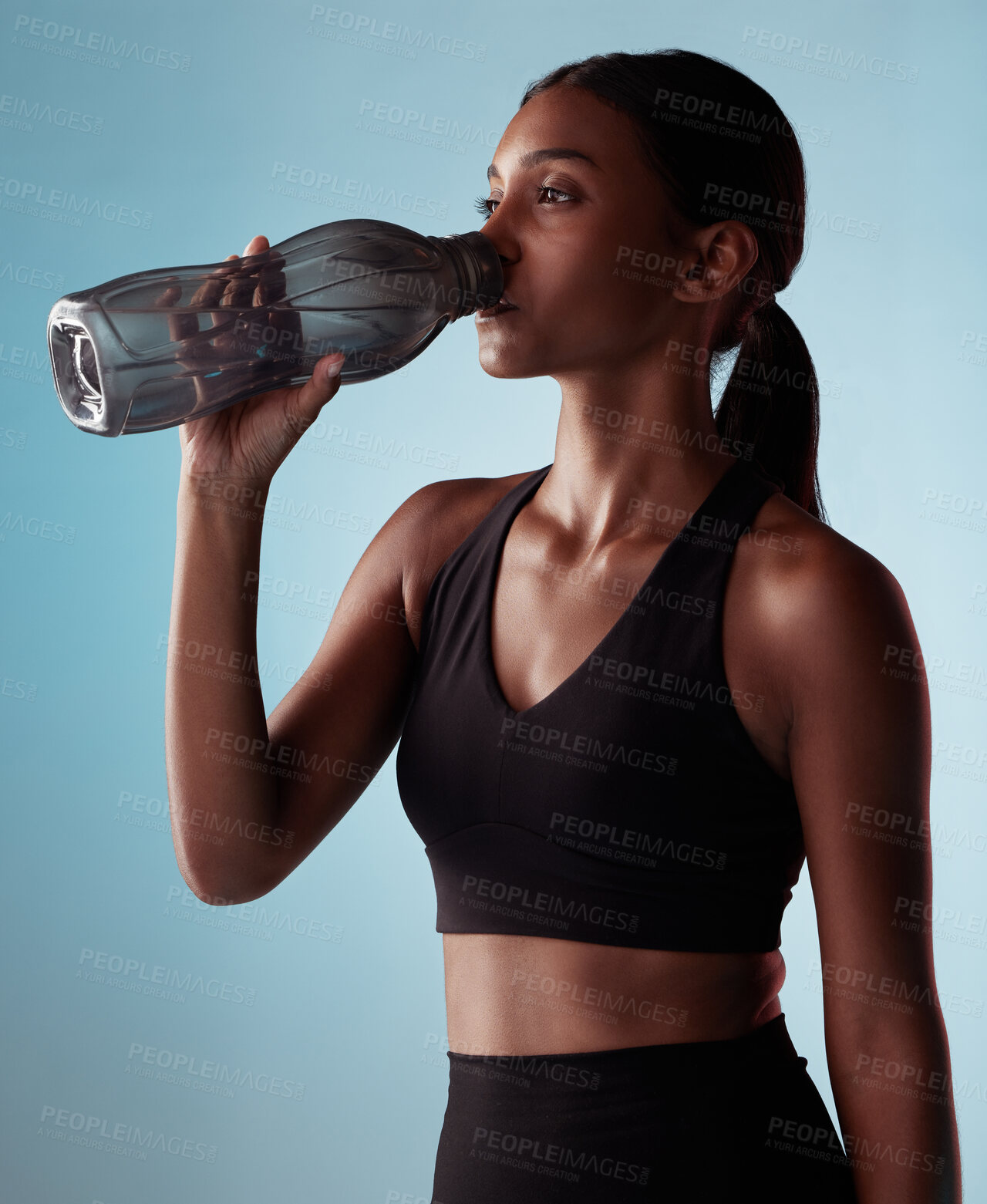 Buy stock photo Fitness woman drinking water bottle in studio, training and workout, exercise or sports challenge on blue background. Thirsty young athlete, hydration rest or wellness, healthy lifestyle or nutrition