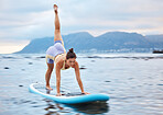 Surfer, flexible and woman on surfboard at a beach training, workout and full body yoga exercise on water in nature. Ocean, surfing and sports girl in a downward dog pose with balance and fitness 