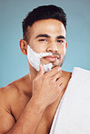 Face, beauty and shave with a man model in studio on a blue background for shaving or grooming. Portrait, skincare and hair removal with a handsome young male shaving his beard in the bathroom