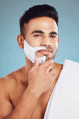 Buy stock photo Face, beauty and shave with a man model in studio on a blue background for shaving or grooming. Portrait, skincare and hair removal with a handsome young male shaving his beard in the bathroom