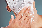 Hand, face and shave with a man applying shaving foam or cream while grooming in studio on a blue background. Skincare, wellness and hair removal with a male in his bathroom to groom his beard
