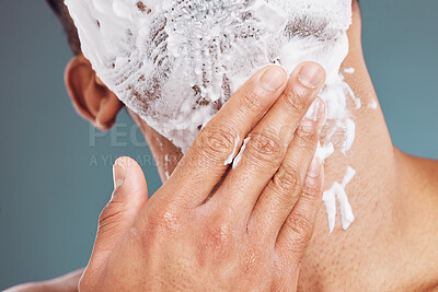 Buy stock photo Hand, face and shave with a man applying shaving foam or cream while grooming in studio on a blue background. Skincare, wellness and hair removal with a male in his bathroom to groom his beard