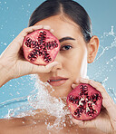 Face, skincare and pomegranate in woman hands with water splash for facial organic, eco friendly or vegan product in studio blue mock up. Model with fruits for glow skin care promotion or advertising