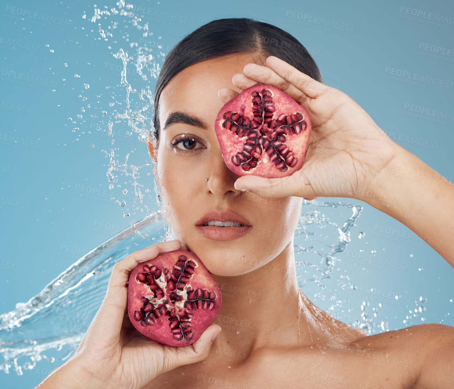 Buy stock photo Pomegranate, skincare and beauty woman with water splash in studio blue mock up for healthy, wellness and skin glow advertising. Young woman with vitamin c fruits for facial product marketing mockup