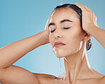Shower, water and woman cleaning her body on a blue studio background. Bodycare, haircare and health or wellness with a young female cleansing her face, getting wet for fresh and cosmetic skin