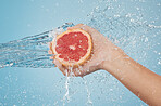 Fruit, water and hand splash for beauty, care and healthy skincare and bodycare on a blue studio background. Grapefruit, hands and hygiene with vitamin c for organic and natural body skin cleansing