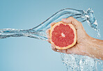 Grapefruit, water and hand with a summer food for health, nutrition and diet against a blue mockup studio background. Splash, tropical and person cleaning a citrus fruit for snack with mock up space