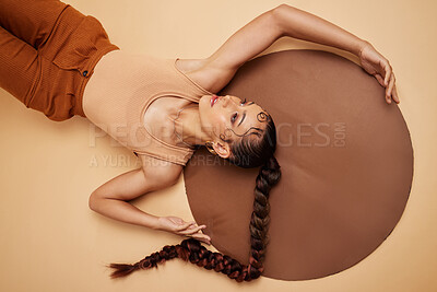 Buy stock photo Creative, art and beauty with a model woman lying in studio on a beige background with a circle prop from above. Fashion, design and artistic with an attractive young female on the ground or floor