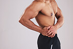 Pain, waist and man with an injury after exercise, fitness and training against a grey studio background. Healthcare, accident and person feeling their body with appendicitis and medical emergency