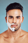 Portrait, skincare and man shaving in studio on blue background for facial hair grooming in India. Healthy, products and young face model shaves beard and mustache in self care routine with cream