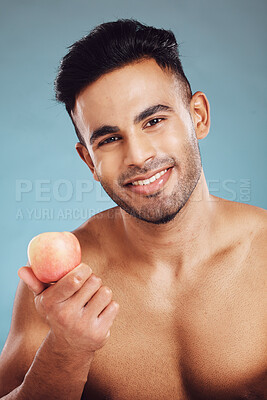 Buy stock photo Apple, fitness and man in a studio portrait before eating healthy fruit on a vegan diet and wellness lifestyle. Nutrition, blue background and happy Indian model enjoying organic vitamins for a snack
