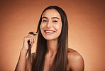 Cosmetics, hair care and young woman pride with natural beauty, healthy and confident with brown studio background. Portrait, makeup and girl playing with hair, wellness and organic for happiness.
