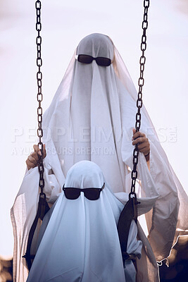 Buy stock photo Halloween, ghost and family wearing white sheet and sunglasses costume at an outdoor park with child on a swing at playground. Horror, scary and celebrate fun holiday with creative woman and kid 