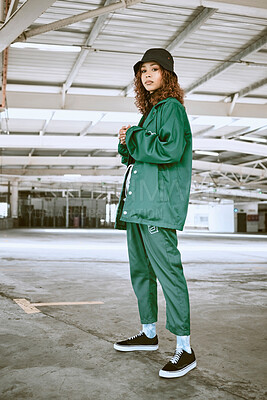 Portrait, fashion and stylish young gen z woman standing in a warehouse  while wearing green clothing. Trendy, hipster latino girl with curly hair  in industrial building or factory with pride or cool |
