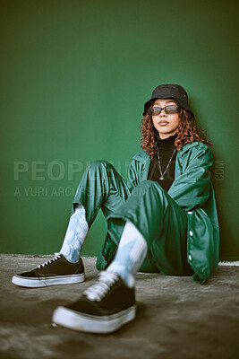 Buy stock photo Fashion, style and clothes with a model black woman sitting on the floor against a green background. Portrait, glasses and fashionable with a young female posing to promote trendy or edgy clothing