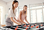 Foosball, women and friends playing table soccer in an office for fun, bonding and competition at work with happiness, energy and motivation. Employees enjoying football game for team building