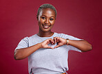 Hands, heart and love with a model black woman in studio on a red background to promote health or wellness. Portrait, smile and hand sign with a young female posing to endorse romance or cardio